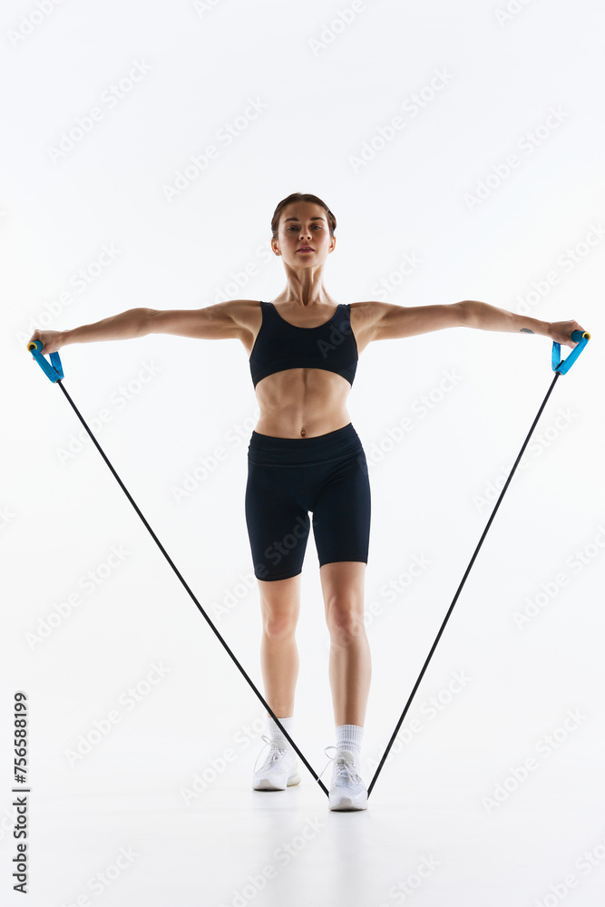 Fit young woman in black sportswear training, using resistance bands for arm exercise isolated over white studio background. Concept of sport, health and body care, fitness app, exercises templates Fit young woman in black sportswear training, using resistance bands for arm exercise isolated over white studio background. Concept of sport, health and body care, fitness app, exercises templates