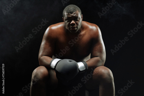 Dramatic backlit portrait of muscular African American boxer looking at camera sitting against black background © Seventyfour