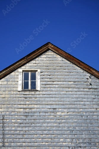 Fassade eines Altbau mit Spitzgiebel, Fassade mit Schindeln aus Schiefer und einsamen Holzfenster vor blauem Himmel im Sonnenschein an der Schifferstraße im Stadtteil Sachsenhausen in Frankfurt am Mai