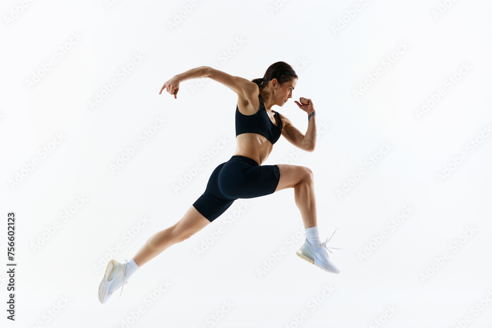 Dynamic image of young woman with strong, healthy, sportive body in sportswear in motion, training isolated over white studio background. Concept of sport, health and body care, fitness app