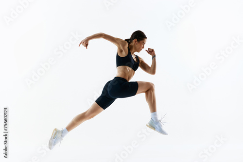 Dynamic image of young woman with strong, healthy, sportive body in sportswear in motion, training isolated over white studio background. Concept of sport, health and body care, fitness app