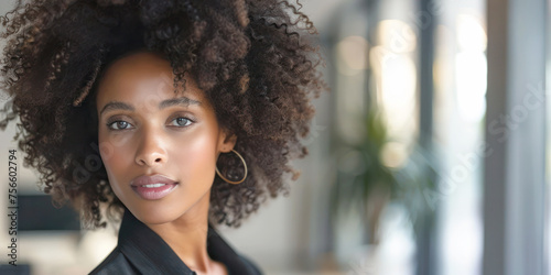 Young Businesswoman Portrait. A close-up portrait of a young, confident African American businesswoman with natural curly hair, wearing a black jacket, set against a modern office backdrop.