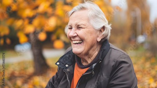 A joyful elderly woman laughing heartily outdoors with autumn leaves in the background.
