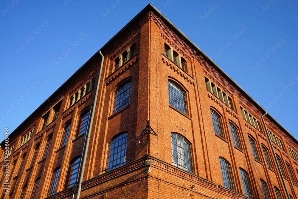 Fototapeta premium Fensterfront einer alten Fabrik mit Fassade aus Backstein vor blauem Himmel im Sonnenschein in der Klassikstadt im Stadtteil Fechenheim in Frankfurt am Main in Hessen