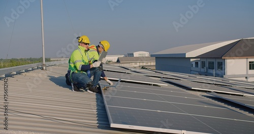 Solar panel technicians Workers in reflective gear are discussing over a laptop on a vast solar array during a bright day sunset sky in the background