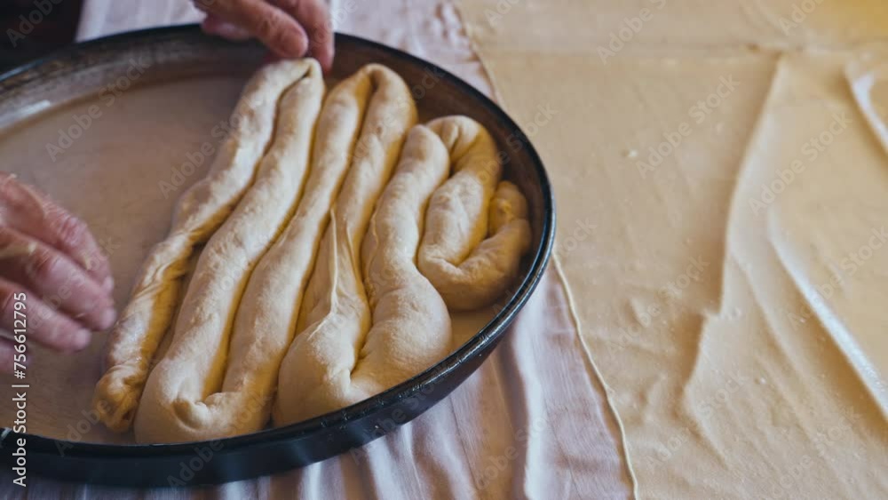 Close-up of old female hands preparing traditional Bosnian and Turkish Borek in the metal baking tray. This dish is featuring savory fillings like cheese, meat, or potato wrapped in flaky filo pastry