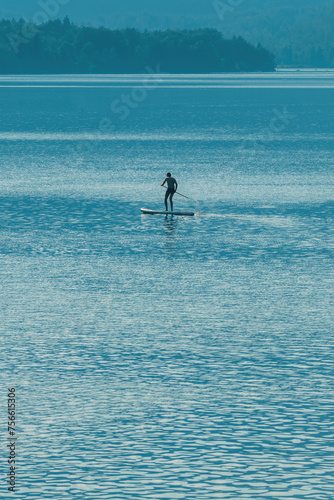 Back lit silhouette of male sportsman paddling standup board on Lake Bohinj in Slovenia