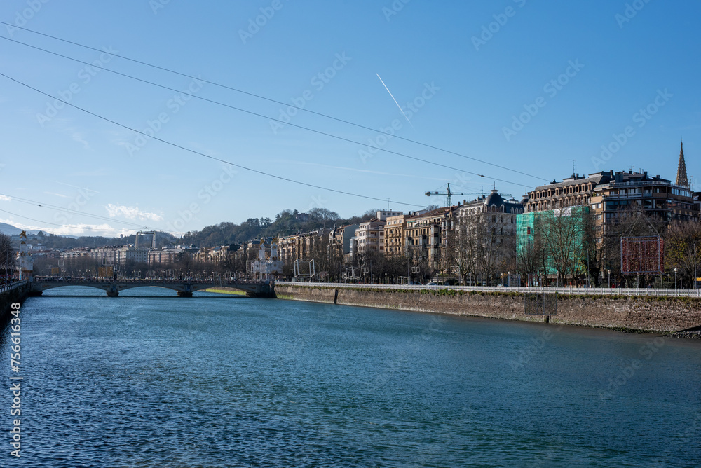 Naklejka premium View of the touristic city of San Sebastian located by the sea on the Basque coast with a large river and full of classical monumental architecture on a sunny day.