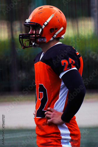 An American football player in an orange and black uniform with the number 22 watches the game 