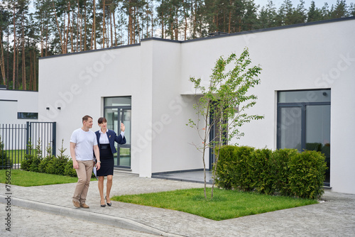 Buyer and sales manager walk through yard of new house © Svitlana