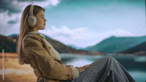 Female working from distance and travelling. Young woman freelancer resting near mountain lake, wearing headphones, listening music.