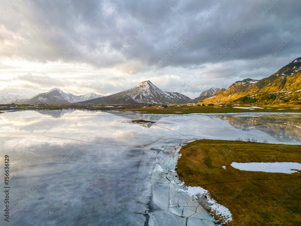 Tranquil landscape with icy lake in the foreground and snow-capped mountains under cloudy skies.