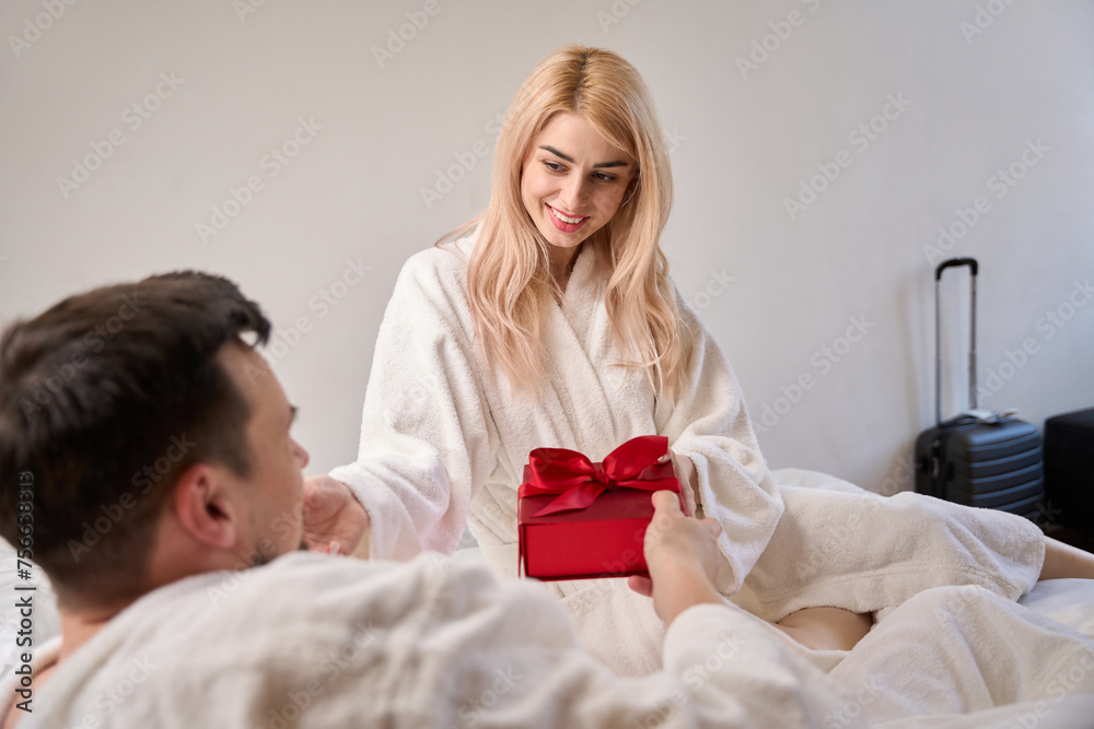 Happy newlyweds are seated in cozy bathrobes on the bed Happy newlyweds are seated in cozy bathrobes on the bed