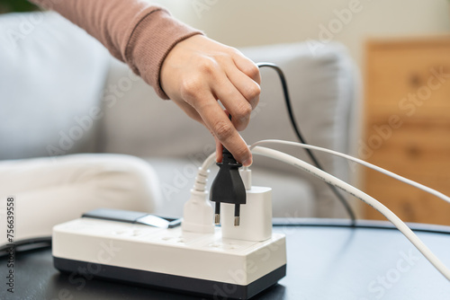 Closed up hand of woman plugged in, unplugged electricity cord cable on socket on table for energy saving, electric power on plate outlet, control expense electrical appliances, environment concept. photo