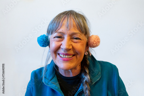 Woman with pompoms over her ears laughing. Person in her sixties with long grey hair and a long plait. Dressed in a blue fleece. Plain background photo