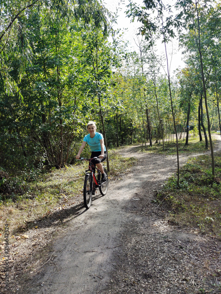 A young blonde woman rides a bicycle through the forest. Front view. Tourism, sports and outdoor recreation