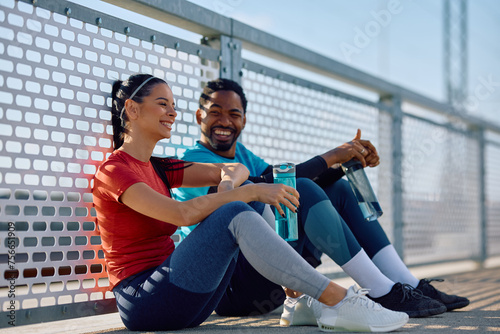 Happy athletic couple relaxing on water break while having sports training outdoors.
