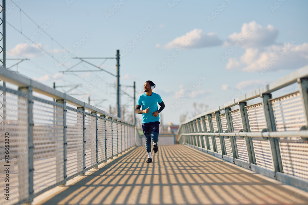 Black male athlete running over the bridge during outdoor sports training.