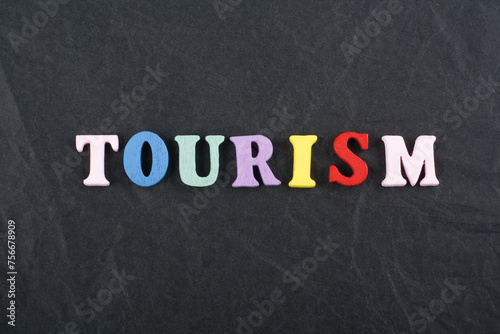 TOURISM word on black board background composed from colorful abc alphabet block wooden letters, copy space for ad text. Learning english concept.