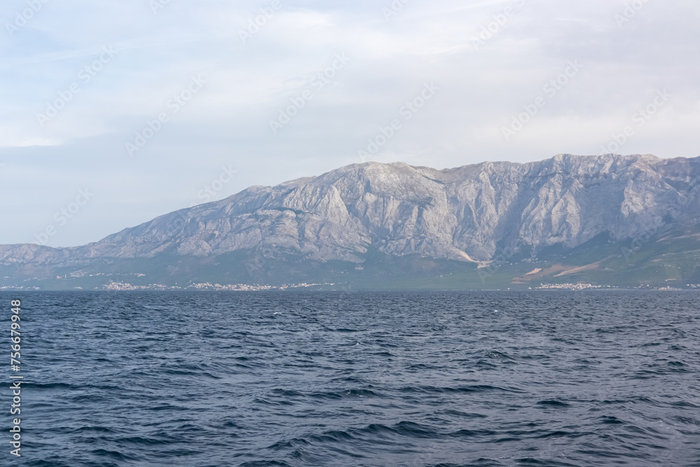 Scenic view of Makarska Riviera with untamed mountain range Biokovo in Dinaric Alps. Majestic coastline of Adriatic Mediterranean Sea in Dalmatia, South Croatia, Europe. Boat tour in Balkan peninsula