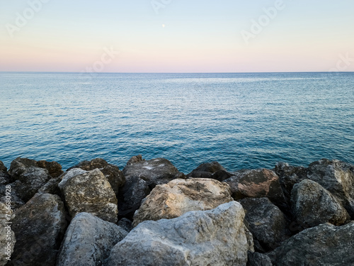 Rippled empty sea, purple, pink, blue sky background texture. Afternoon at rocky beach, copy space.