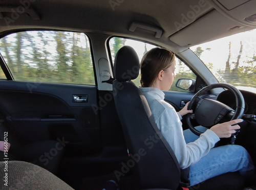 Young traveler girl driving her grand tourer car on the roads. She is driving attentively with her hands on the wheel, it is daytime and she is driving a very large car. Interior view © Adolf