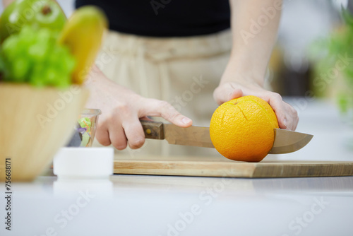close up young woman hands cutting orange and cooking salad in the kitchen