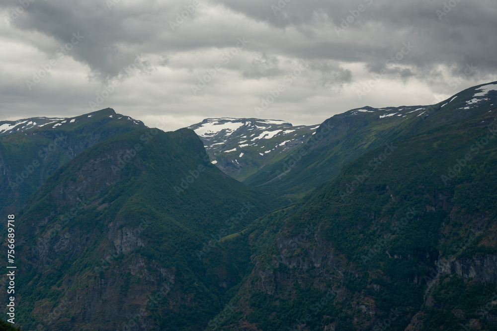 Nature view of Norwegian mountains with white snow cover on its high ground from stegastein viewpoint on a cloudy summer day. Blue uv radiation on the mountains. Nature view of Norwegian mountains with white snow cover on its high ground from stegastein viewpoint on a cloudy summer day. Blue uv radiation on the mountains.