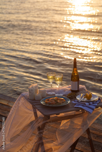 Romantic sunset dinner on the beach. Table honeymoon set for two with luxurious food, glasses of champagne drinks in a restaurant with sea view. Summer love, romance date on vacation concept. © Julhabiby
