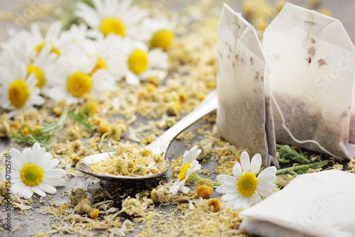Dried chamomile herbal tea in a spoon with paper tea bags and flowers on black background, closeup, healing drink, natural medicine and naturopathy concept photo