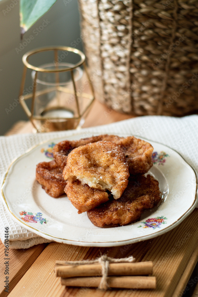 White plate with a torrija, typical dessert of the spanish holy week, it is fried bread with sugar. With some branches of cinnamon on a wood. White plate with a torrija, typical dessert of the spanish holy week, it is fried bread with sugar. With some branches of cinnamon on a wood.