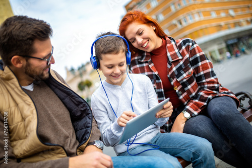 Family sitting on bench, relaxing using gadget, browsing internet.