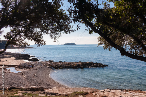 Panoramic view of small islands seen from pebble beach in coastal town Funtana, Istria, Croatia. Calm sea surface of Adriatic Mediterranean Sea in morning hours. Seaside vacation concept in summer photo