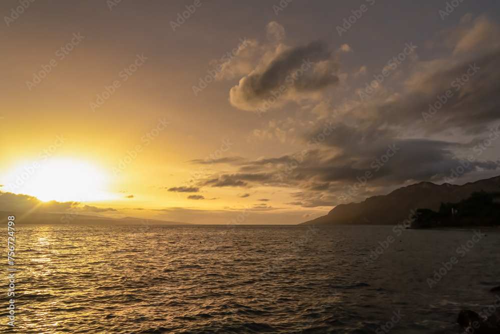 Naklejka premium Enjoying romantic sunset at Punta Rata beach in idyllic town Brela, Makarska Riviera, Dalmatia, Croatia. Dreamlike atmosphere at Adriatic Mediterranean Sea. Sky turning in vibrant red orange colours