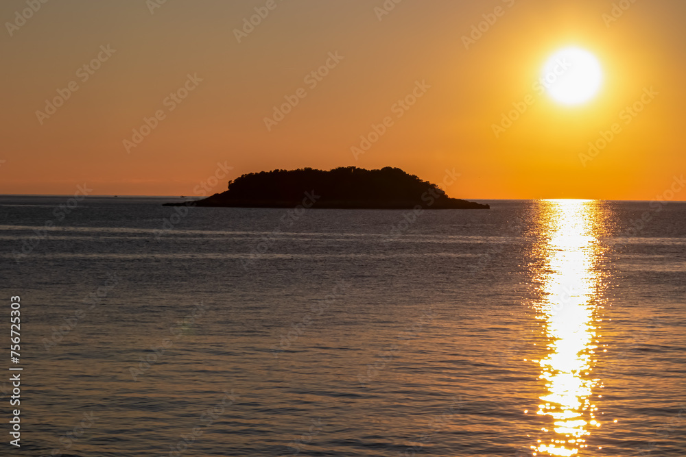 Watching dramatic sunset at coastal village Funtana, Istria, Croatia, EU. Silhouette of remote tropical island. Calm sea surface reflects vibrant colors of sky. Vacation at Adriatic Mediterranean Sea