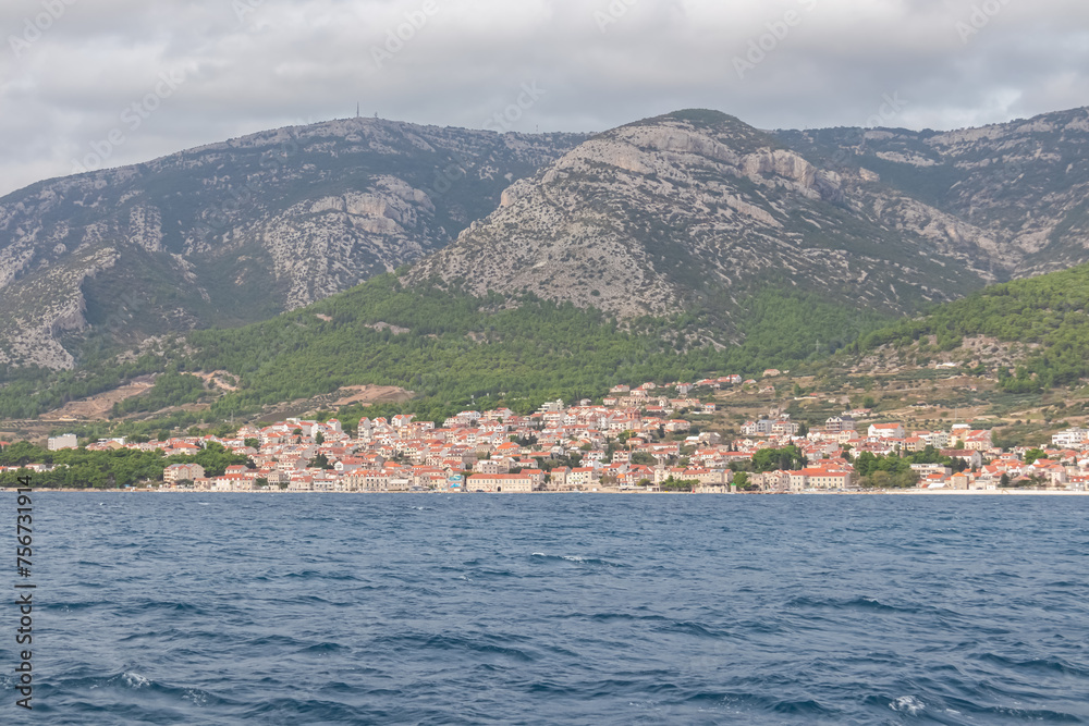 Panoramic view of idyllic coastal town Makarska, Dalmatia, Croatia. Majestic coastline of Adriatic Mediterranean Sea. Untamed mountain range Biokovo in Dinaric Alps. Boat tour in Balkans in summer