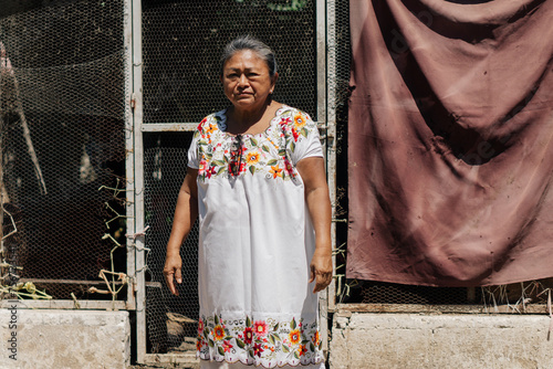 Portrait of a latina woman outside a chicken coop standing on a sunny day looking at the camera.