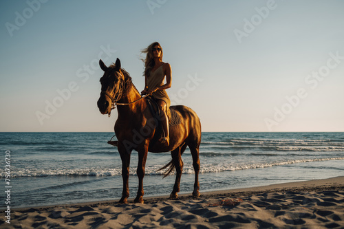 Full length of a young woman horseback riding on a beach at sunset. © Zamrznuti tonovi