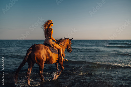 Rear view of a tattooed woman horseback riding at the seaside at sunset.