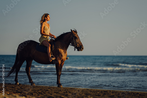 Profile view of an attractive woman riding a horse at sunset on a beach.