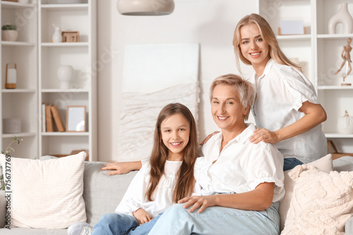 Little girl with her mom and grandmother sitting on sofa at home