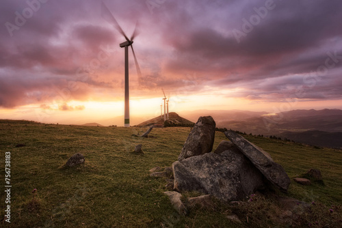 Destroyed dolmen on Mount Oiz, Bizkaia, in the background wind turbines under a warm and dramatic sky at sunset photo