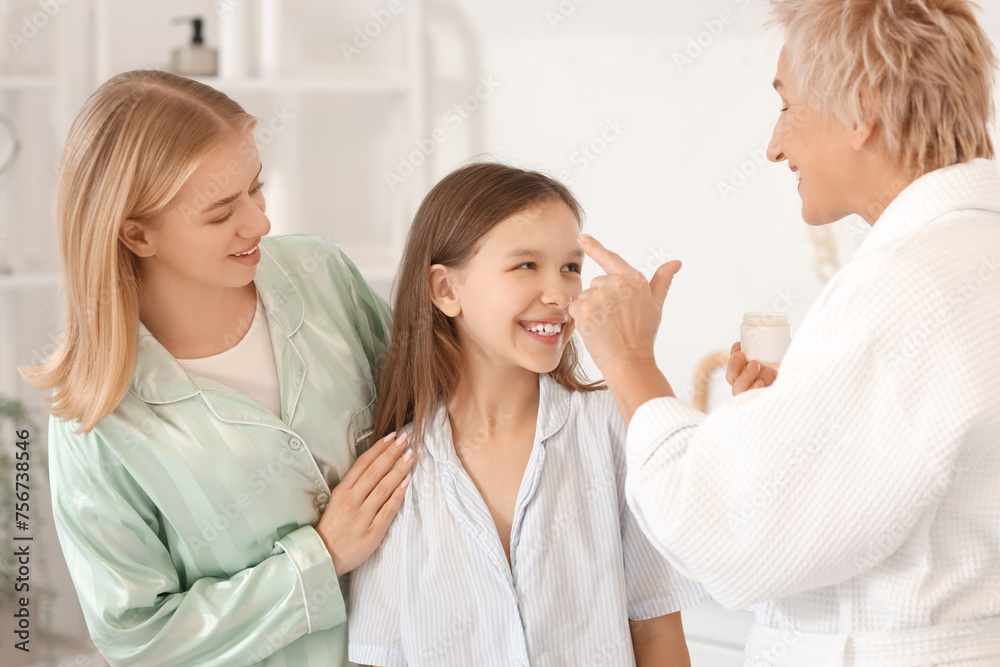 Little girl with her mom and grandmother applying facial cream in bathroom Little girl with her mom and grandmother applying facial cream in bathroom