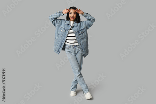 Beautiful young happy Asian woman in stylish denim clothes on grey background