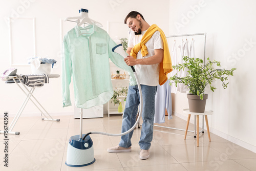 Happy young man steaming green shirt and talking by mobile phone in laundry room