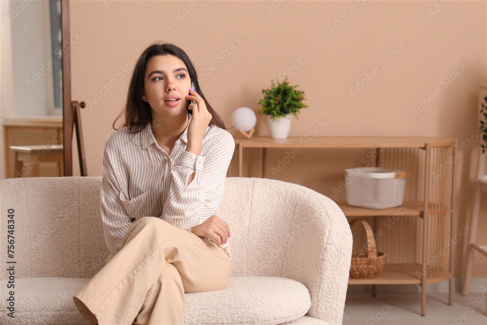 Beautiful young woman sitting on comfortable sofa and talking by mobile phone in living room at home Beautiful young woman sitting on comfortable sofa and talking by mobile phone in living room at home