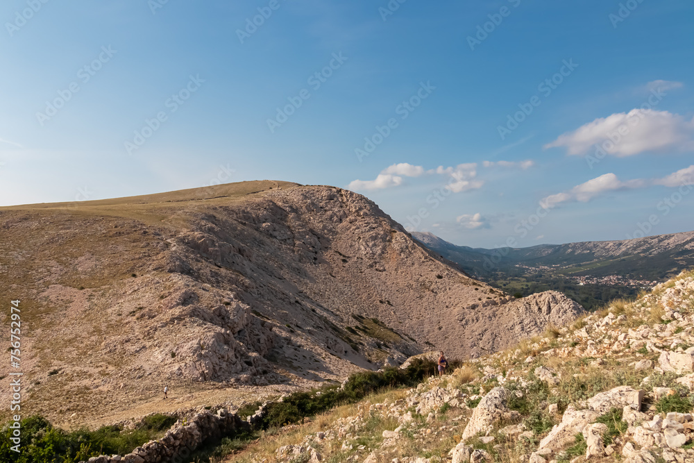 Woman on idyllic hiking trail with scenic view of majestic highlands and hills near coastal town Baska, Krk Island, Primorje-Gorski Kotar, Croatia, Europe. Aerial vistas from mountains in summer