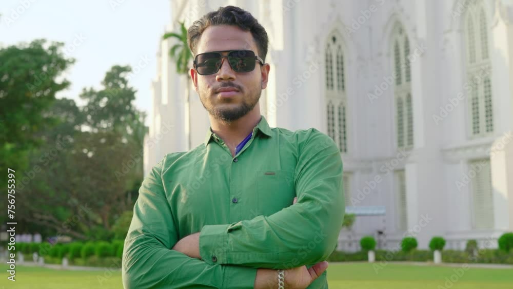 A young cool hipster confident Indian Asian man or male with crossed arms and wearing sunglasses standing outdoors in front of the church or white building looking or facing the camera on a sunny day A young cool hipster confident Indian Asian man or male with crossed arms and wearing sunglasses standing outdoors in front of the church or white building looking or facing the camera on a sunny day