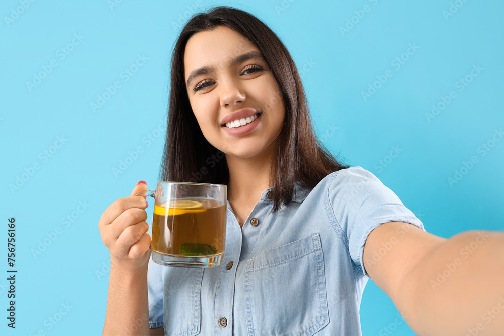 Young woman with glass cup of lemon tea taking selfie on blue background, closeup Young woman with glass cup of lemon tea taking selfie on blue background, closeup