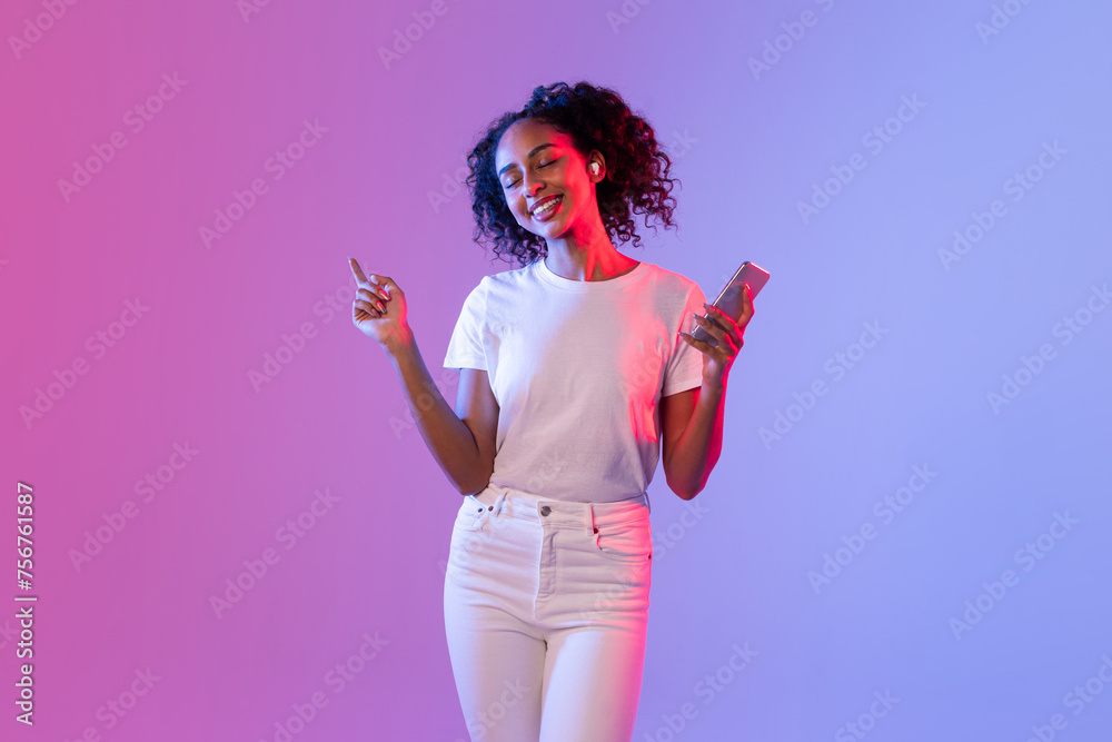 Happy lady with smartphone and earbuds enjoying music on colorful background
